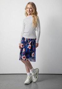 Pasiasty, długi rękaw top z czerwonymi akcentami, w połączeniu z kwiecistą, do kolan sukienką w odcieniach niebieskiego, różowego i czerwonego, noszoną z białymi skarpetkami i trampkami.