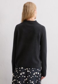 Schwarzer Wollpullover mit hohem Kragen und langen Ärmeln, mit lockerem Sitz und glatter Textur, kombiniert mit einem floralen Rock.