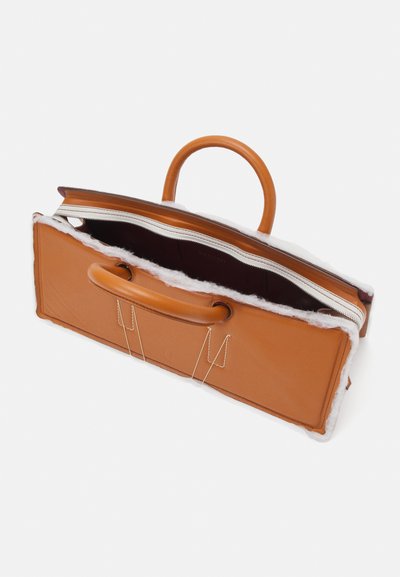 Rjava usnjena torba z mehkim belim podlogom. Ima dva ročaja in zadrgo. Pravokotna oblika z razkritimi šivi.