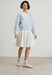 Light blue sweatshirt with a round neckline, paired with a white pleated skirt. White sneakers with gum soles and grey socks.
