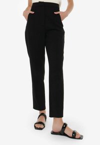 Pantalons noirs ajustés avec une taille haute, des poches latérales et une coupe slim. Tissu lisse, longueur courte, associés à des sandales noires plates.