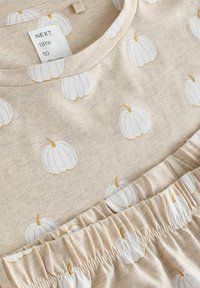 Ljusbeige topp med vit pumpamönster och guld detaljer. Har en rund halsringning och rynkig textur vid fållen. Mjuk tygmaterial.