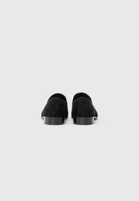 Musta mokka loafers, joissa on matala pino heeled, pyöristetty varvas ja minimalistinen muotoilu. Sujuva pinta, jossa on hienovaraisia ompeluja.