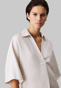 Lichtbeige blouse met korte mouwen, een sjawlkravery en een losse pasvorm. Gladde stof met een subtiele textuur en een diepe V-hals.