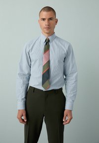 Hellblau gestreifte Hemd mit dunklegrüner Hose und einer mehrfarbigen Krawatte mit diagonalen Streifen in Pink, Grün und Blau.