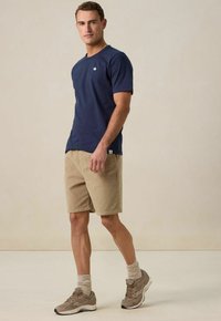 Marineblauwe katoenen T-shirt met korte mouwen, tankleurige shorts en grijze sneakers. Bevat een klein logo op het T-shirt en beige gestructureerde sokken.