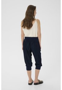 Pantaloni cropped blu navy, larghi e con vita elastica; modella che indossa una canotta beige chiaro e scarpe nere senza lacci.