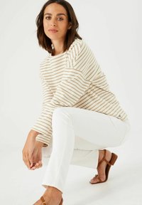 Camiseta de manga larga a rayas en beige y crema, combinada con jeans blancos. Sandalias marrones con una pequeña correa y un detalle de hardware sutil.