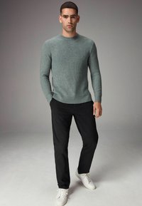 Pulover gri tricotat cu un model texturat, guler rotund, asociat cu pantaloni negri și adidași albi. Aspectul general este casual și ajustat.
