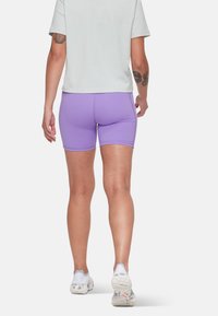 Lila cykelbyxor gjorda av elastiskt material, med en tajt passform och kontrasterande sömmar. Bärs tillsammans med en ljus t-shirt och träningsskor.