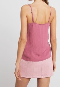 Top senza maniche rosa con una finitura testurizzata, spalline regolabili, abbinato a una gonna di jeans rosa chiaro con orlo sfilacciato.