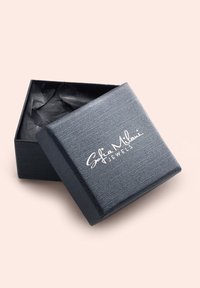 Svart smyckeskrin med en texturerad yta, försett med en vit logotyp "Sofia Milani Jewels." Locket är något på glänt och avslöjar svart silkespapper inuti.