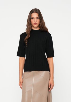 Svart ribbestrikket genser med korte ermer og høy hals, kombinert med en beige plisserte skjørt. Myk tekstur og tettsittende design.