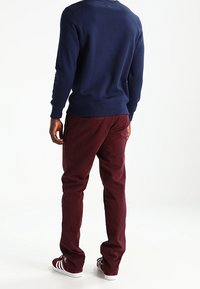 Felpa blu navy con polsini e orlo a costine, abbinata a pantaloni bordeaux. Le scarpe presentano strisce bianche su uno sfondo rosso.