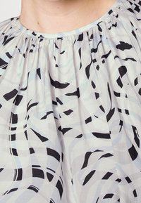 Lätt, mönstrad topp i mjukt tyg med svarta och blå abstrakta virvlar på en ljus bakgrund; rynkad halslinning.