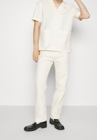 Korte mouwen, knoopsluiting shirt van gestructureerde crèmekleurige stof, gecombineerd met crèmekleurige rechte broek en zwarte instappers. Bevat twee voorzakken.