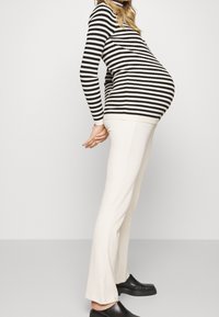 Maglione a righe bianco e nero in maglia con design aderente, abbinato a pantaloni a gamba larga color crema a coste e scarpe slip-on nere.