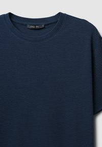 T-shirt textured di colore blu navy con scollatura rotonda, maniche corte e un'etichetta sul colletto. Presenta un motivo intrecciato sul tessuto.