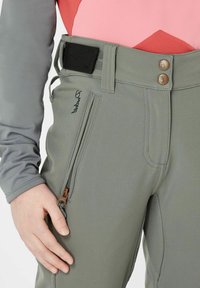 Graue Outdoor-Hosen mit glatter Textur, ausgestattet mit einer Reißverschlusstasche, zwei bronzefarbenen Knöpfen und einem verstellbaren Bund mit einem schwarzen Klettverschlussriemen.
