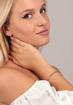 Bracciale argento elegante con accenti viola, poggiato su un polso nudo. La modella posa con una mano sul collo, indossando una maglietta bianca a spalle scoperte.