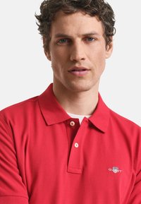 Polo shirt rossa con un design classico, dotata di un colletto a tre bottoni e logo ricamato sul petto. Realizzata in un tessuto testurizzato.