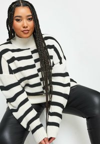 Dicker gestreifter Pullover in Creme und Schwarz, gerippter Rollkragen, weit geschnitten, lange Ärmel, kombiniert mit schwarzen Lederhosen.