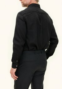 Zwarte blouse met lange mouwen en een klassieke kraag, met voor- en achterrugdetails en knopenmanchetten, gecombineerd met donkere, op maat gemaakte broeken.