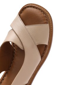 Sandal in pelle beige con design a fascia incrociata, texture liscia e soletta marrone con dettagli appuntati lungo il bordo.