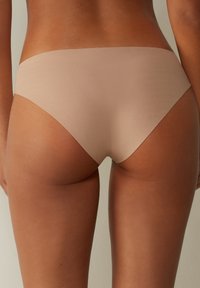 Beige naadloze ondergoed met een gladde textuur, een lage taille en een minimalistische snit, zonder zichtbare naden of hardware.