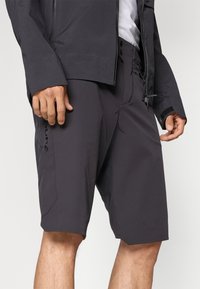 Pantalones cortos grises fabricados con tejido texturizado, que cuentan con un ajuste holgado, bolsillos laterales y un sutil branding en la pierna izquierda.