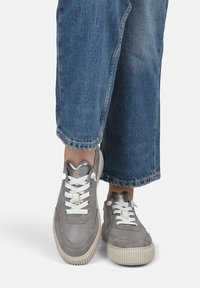 Baskets grises en daim texturé et cuir lisse, avec des lacets blancs, une semelle nervurée et des accents métalliques sur la languette.