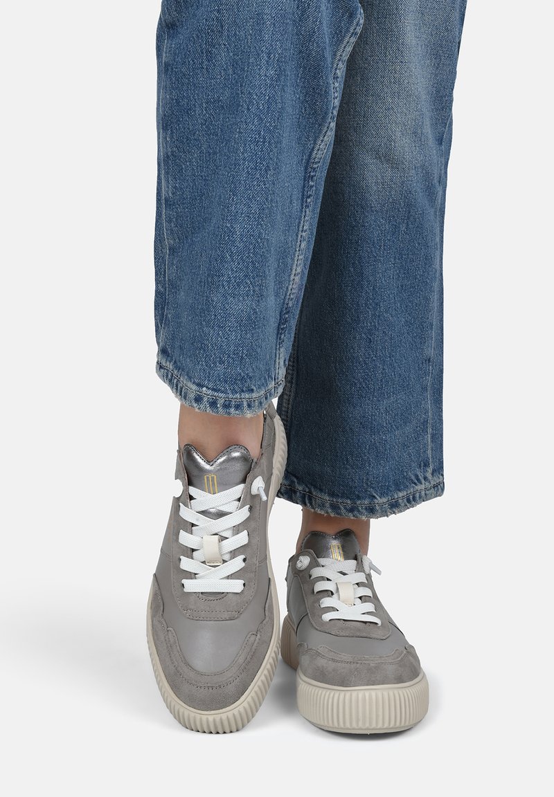 Baskets grises en daim texturé et cuir lisse, avec des lacets blancs, une semelle nervurée et des accents métalliques sur la languette.