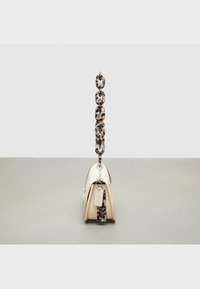 Beżowa skórzana torebka o fakturowanej powierzchni, z ozdobnym łańcuszkowym paskiem z wzorem oraz małą przywieszką. Kompaktowy, usztywniony kształt.