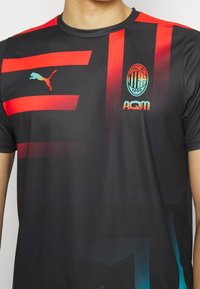 Černé sportovní tričko s červenými a modrými gradientními pruhy, logo Puma na levé hrudi a emblém AC Milan. Krátké rukávy a kulatý výstřih.