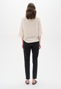 Beige pletený top s širokými rukávy, v kombinaci s černými kalhotami na míru. Hladká textura, minimalistický design, žádné viditelné vzory ani akcenty.