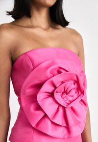Fuchsia stroppeløs topp med en stor teksturert blommedetalj laget av glatt satin. Skreddersydd passform fremhever silhuetten.