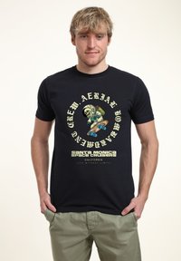 Mladý muž ve černém tričku s grafikou kostlivce astronauta, který skateboarduje, a nápisem "Santa Monica Space Cruisers California."