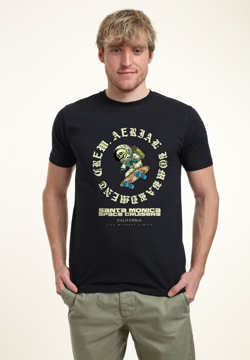 Mladý muž ve černém tričku s grafikou kostlivce astronauta, který skateboarduje, a nápisem "Santa Monica Space Cruisers California."