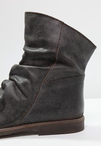 Botte en cuir gris foncé, souple, à surface texturée. Présente une semelle marron unie et une couture simple le long des coutures.