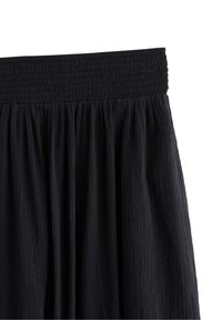 Gonna nera con vita elastica arricciata, caratterizzata da un tessuto strutturato e fluido. Il materiale appare leggero e a strati.