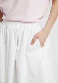 Jupe en coton blanc avec une taille élastique et une poche latérale, présentant une texture de tissu douce et une silhouette fluide.