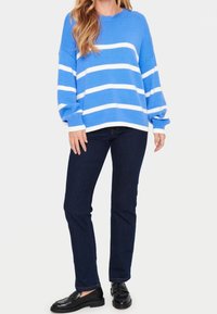 Pull rayé bleu avec des rayures horizontales blanches, texture côtelée et col rond, associé à un jean slim bleu foncé et des mocassins noirs.