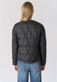 Giacca a piumino nera con motivo trapuntato, scollo rotondo e maniche lunghe. Abbinata a jeans denim azzurro, con una vestibilità comoda.