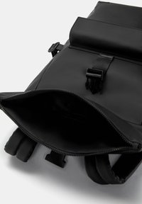 Czarny plecak o strukturalnym designie, wykonany z gładkiego materiału. Posiada regulowane ramiączka, zamek błyskawiczny oraz zapięcie na klapkę.