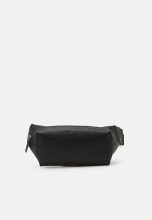 Sort tekstureret læder Calvin Klein bæltetaske med lynlås og justerbar rem på hvid baggrund.