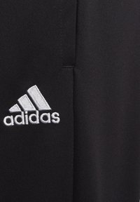 Pantalons de sport noirs en tissu texturé, arborant un logo Adidas brodé blanc bien visible. Design simple et épuré.