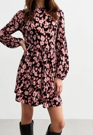 Mujer con un vestido de manga larga, estampado floral en rosa y negro, con cintura fruncida, combinado con botas negras hasta la rodilla.