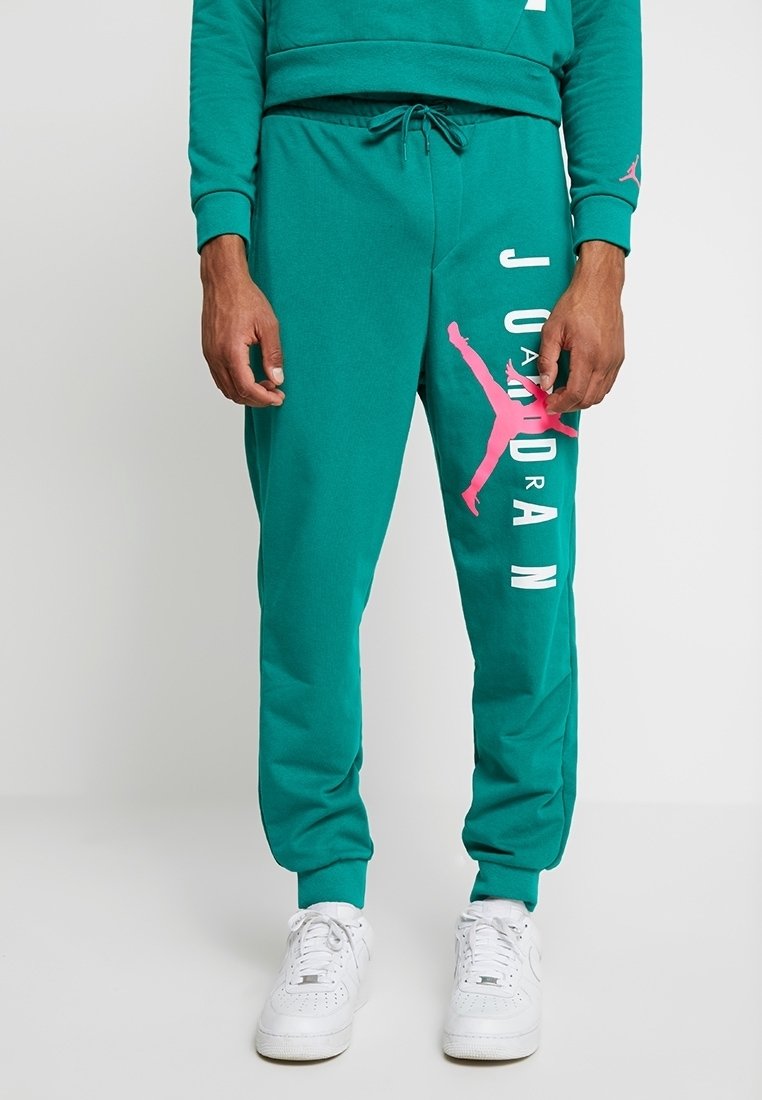 Teal sweatpants i mjukt material, med en vit "JORDAN"-tryck och rosa Jumpman-logotyp på sidan. Elastiska muddar och justerbar dragsko.