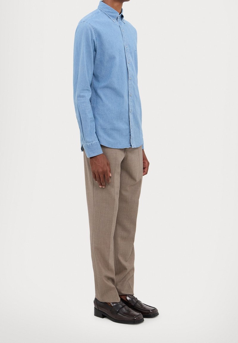 Chemise en jean bleu clair à boutons, manches longues, avec col. Associée à un pantalon beige et des mocassins noirs. Design simple et ajusté.