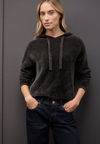 Hoodie grigio scuro e peloso con cappuccio regolabile e polsini a coste, abbinato a jeans blu scuro con chiusura a bottone e tasche frontali.